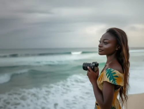 Photographie de l'artiste Inès Konaté tenant son appareil photo devant l'océan