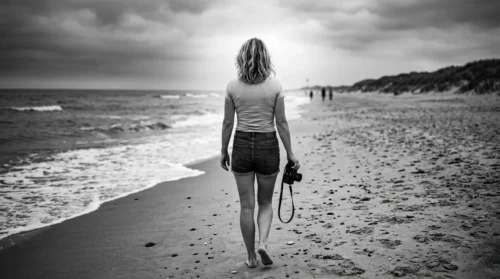 Photographie en noir et blanc de l'artiste Sigrid Voll marchant de dos sur une plage